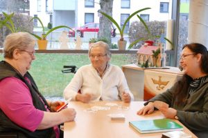 Ehrenamtliche spielt Karten mit Bewohnerinnen im Altenpflegeheim